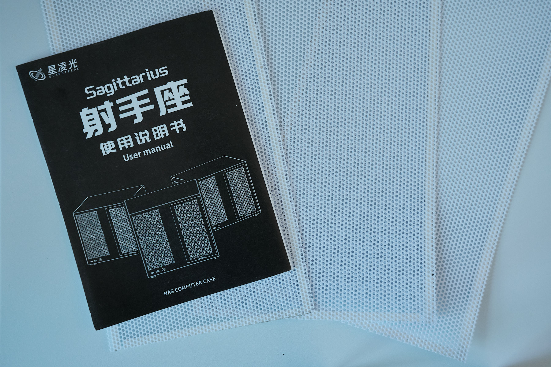The Sagittarius NAS case user manual, a black booklet with Chinese and English text, resting on top of the included white mesh dust filters