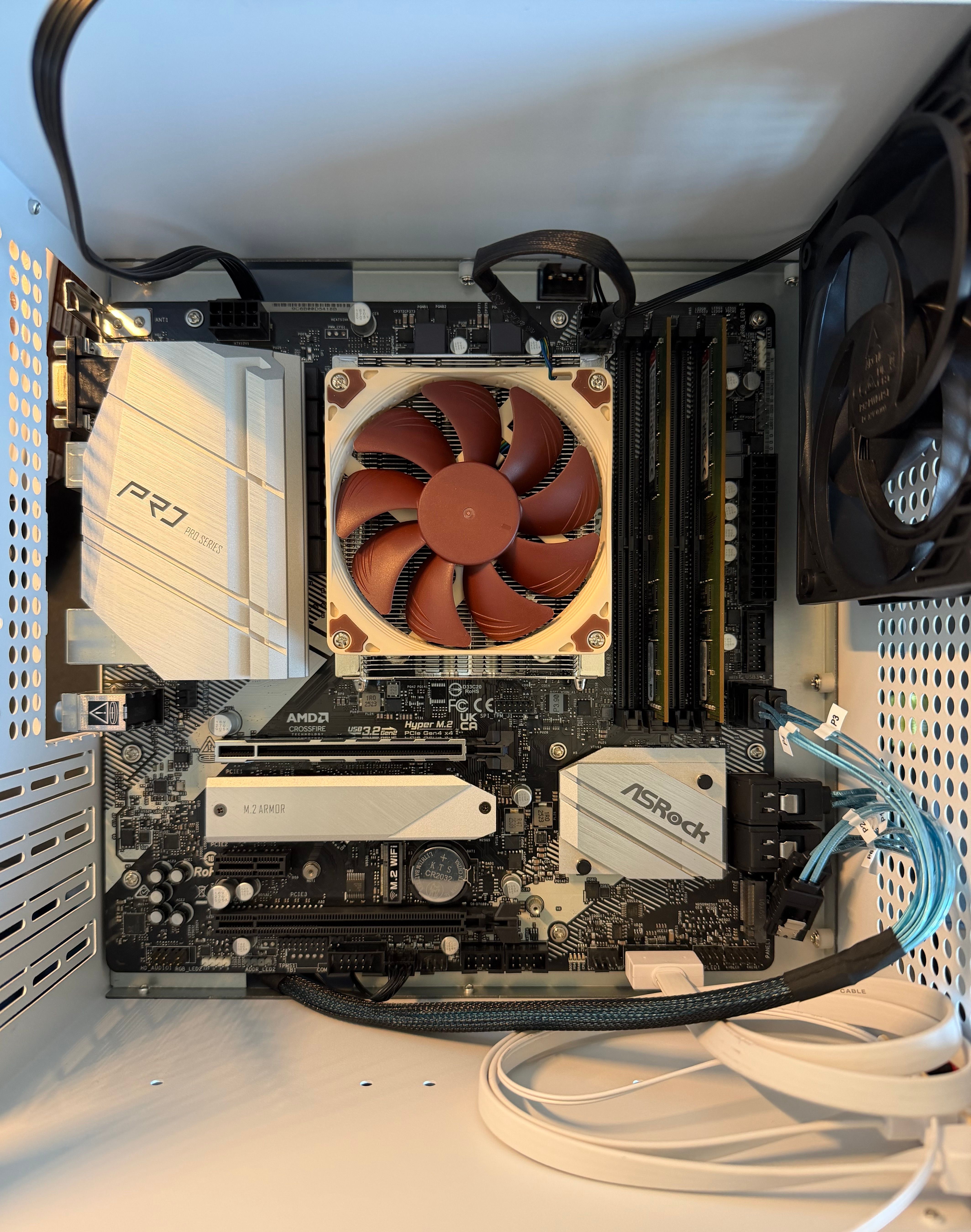 Top-down view of the ASRock B550M Pro4 motherboard installed in the NAS case with RAM sticks, a low-profile Noctua CPU cooler, and a case fan.