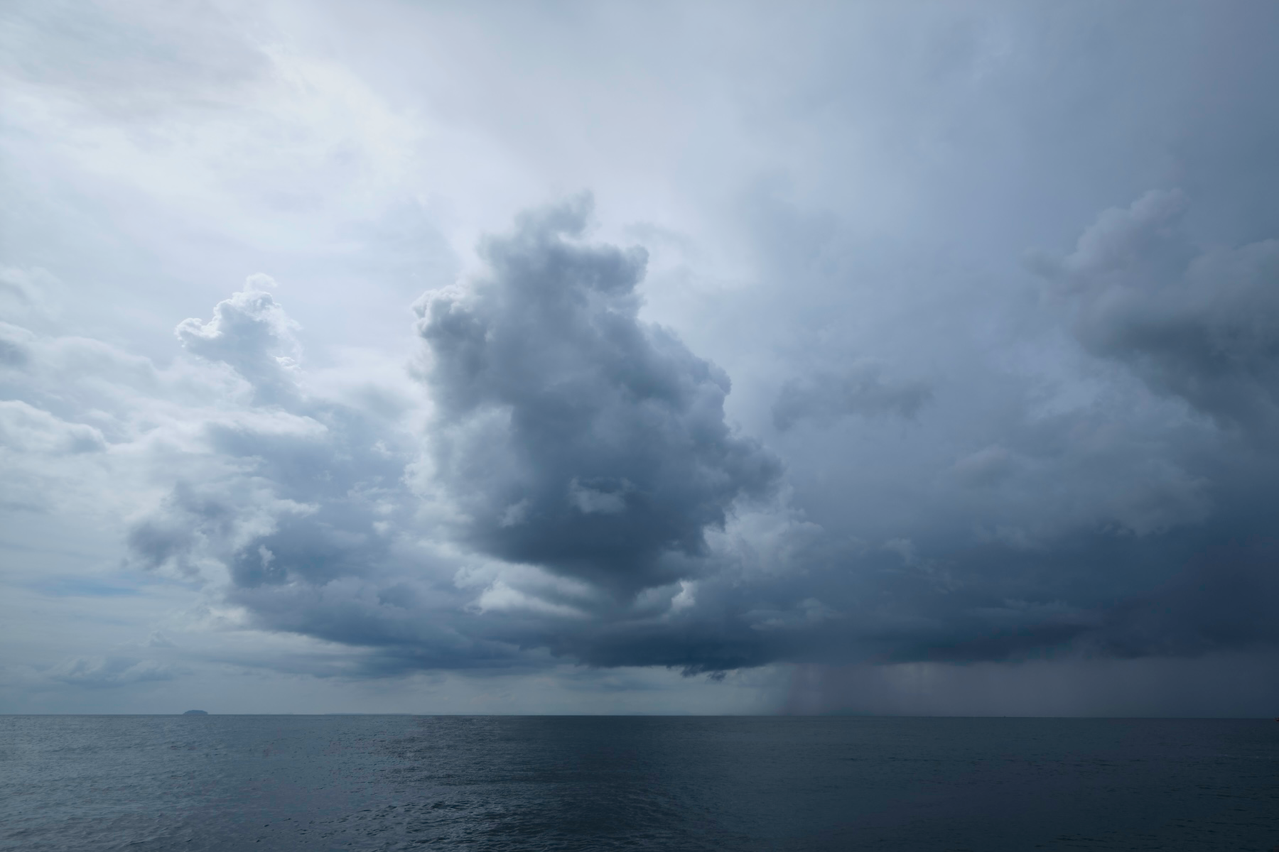 Storm clouds gathering over a dark ocean, with visible rain in the distance.
